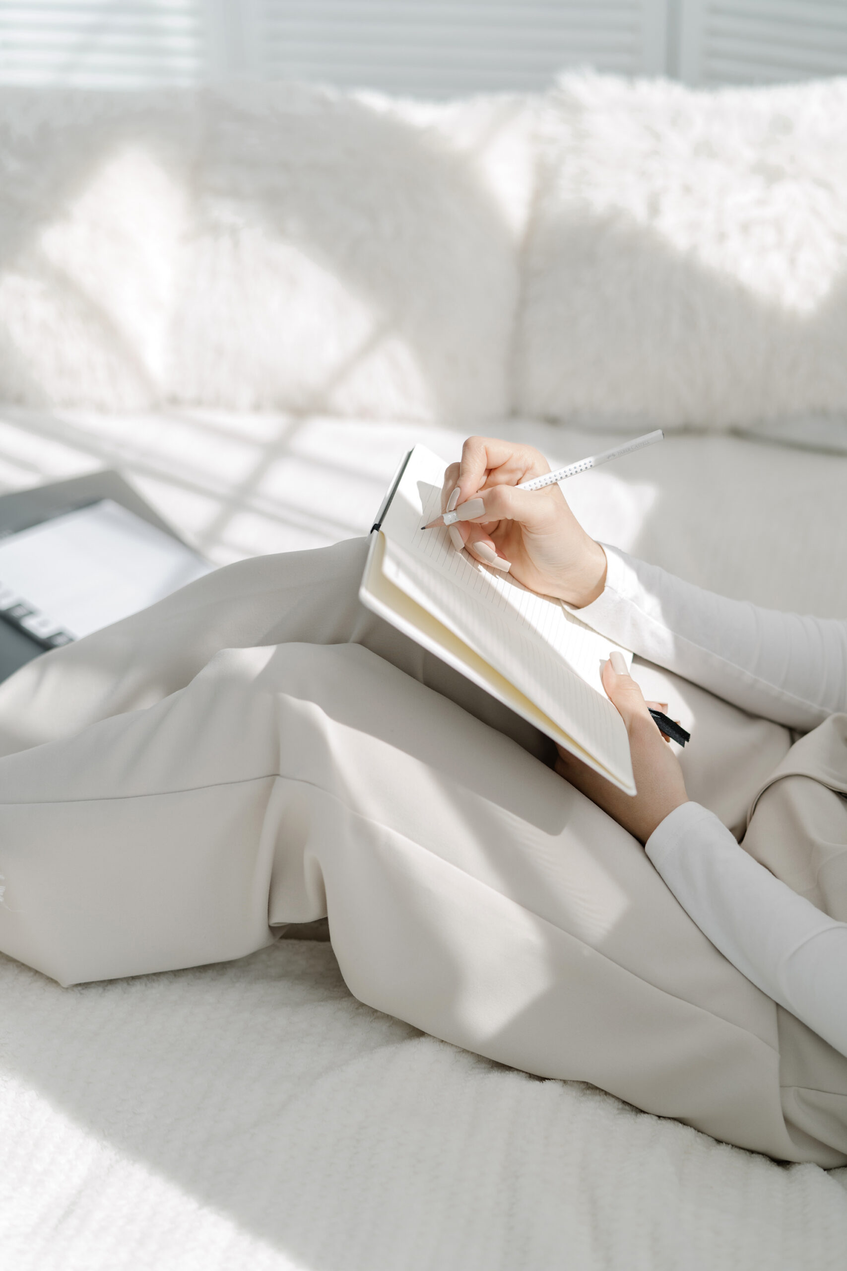 Woman in comfy sweats journaling on white couch